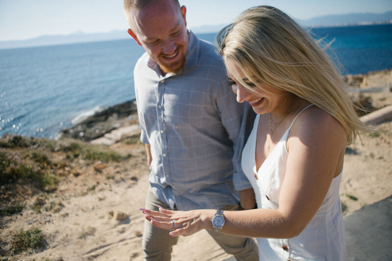 Joyful engagement photo on rocky coastline — candid couple moment during proposal session with sea view