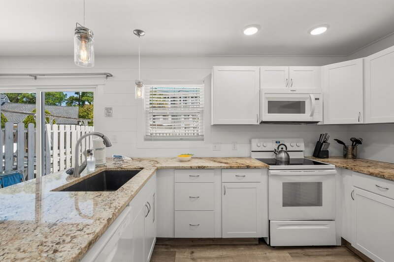 Modern white kitchen at Tropical House featuring granite countertops, full appliances, and natural light, ideal for 30A family rentals.