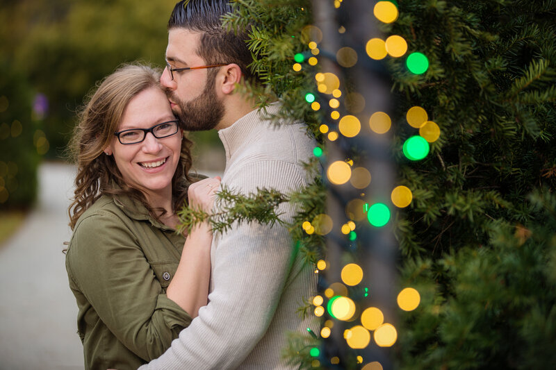 A couple playfully embracing amidst the dazzling Christmas lights at Longwood Gardens during their engagement session, capturing the festive magic and joy of the holiday season.