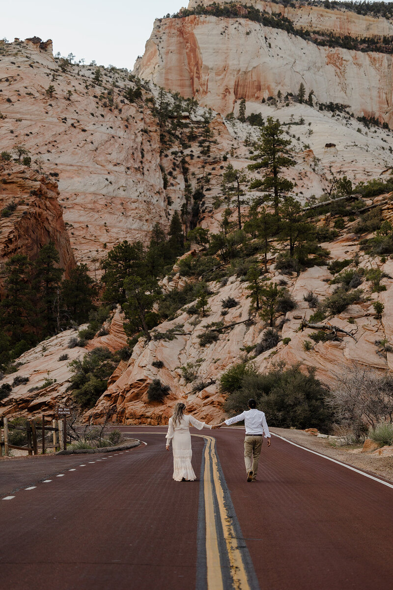 A couple holding hands while walking on the road at Zion National Park. Utah Elopement Photographer