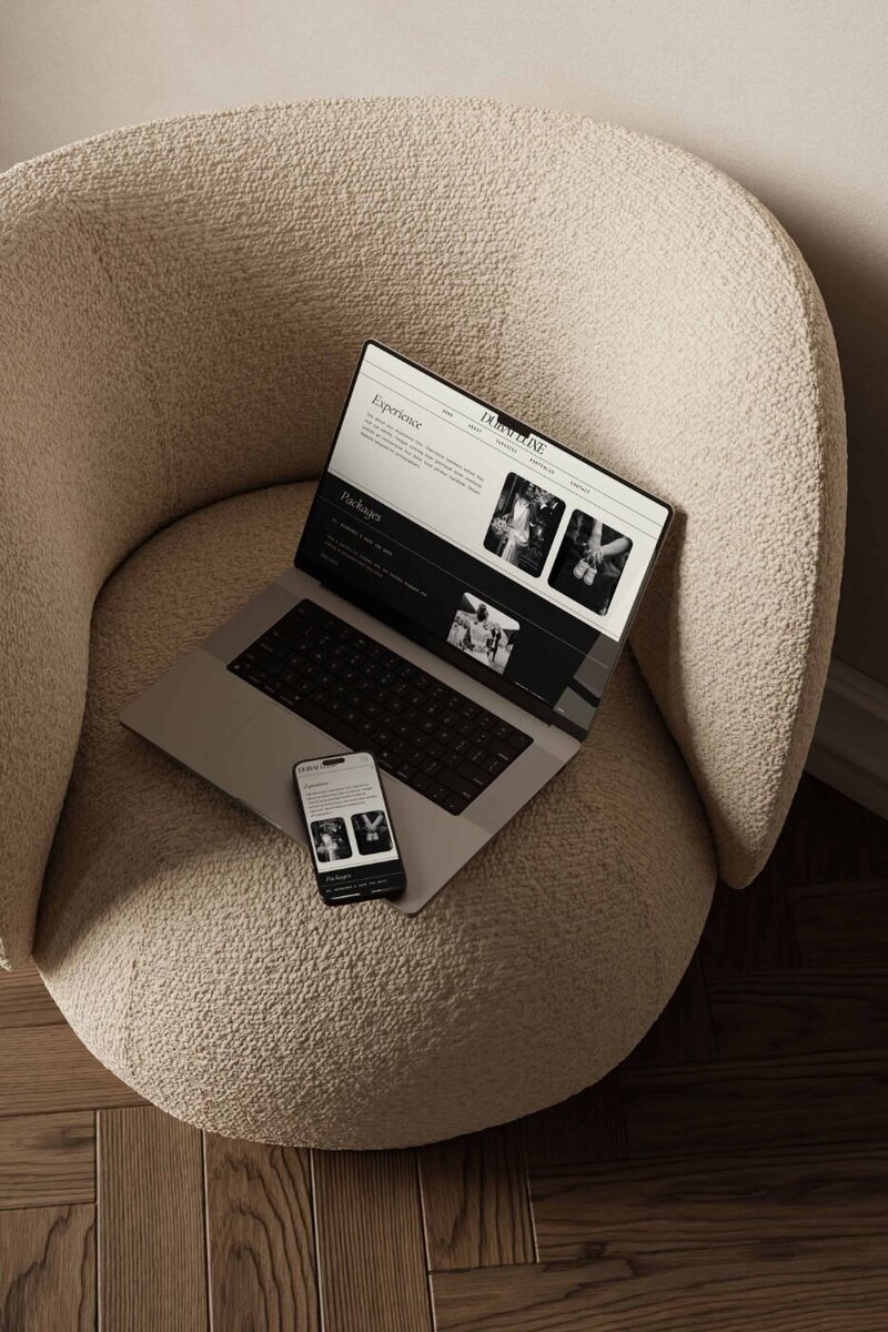 Laptop and smartphone placed on a cream boucle armchair, both screens showing a black-and-white themed wedding photography website “Experience” and “Packages” page