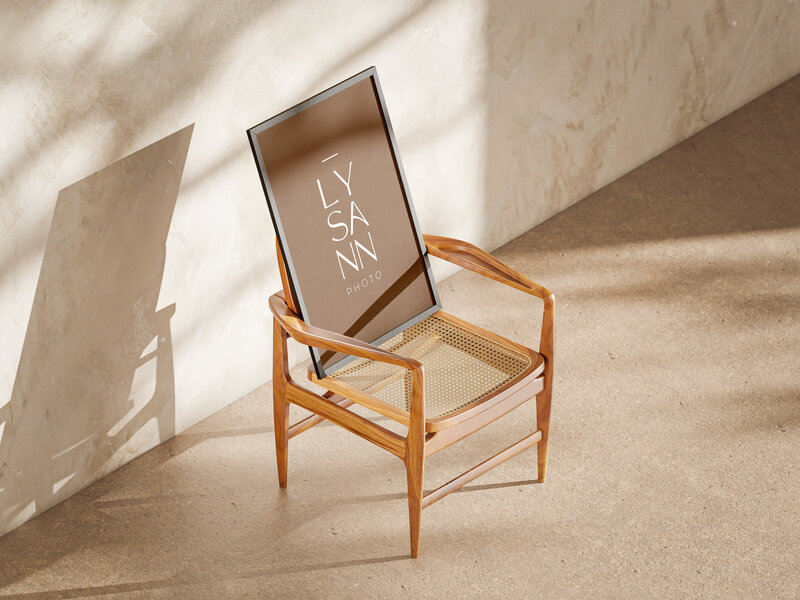 Mockup of a poster sitting on a designer chair in a studio, on the poster in the minimal, elegant logo of a wedding photographer