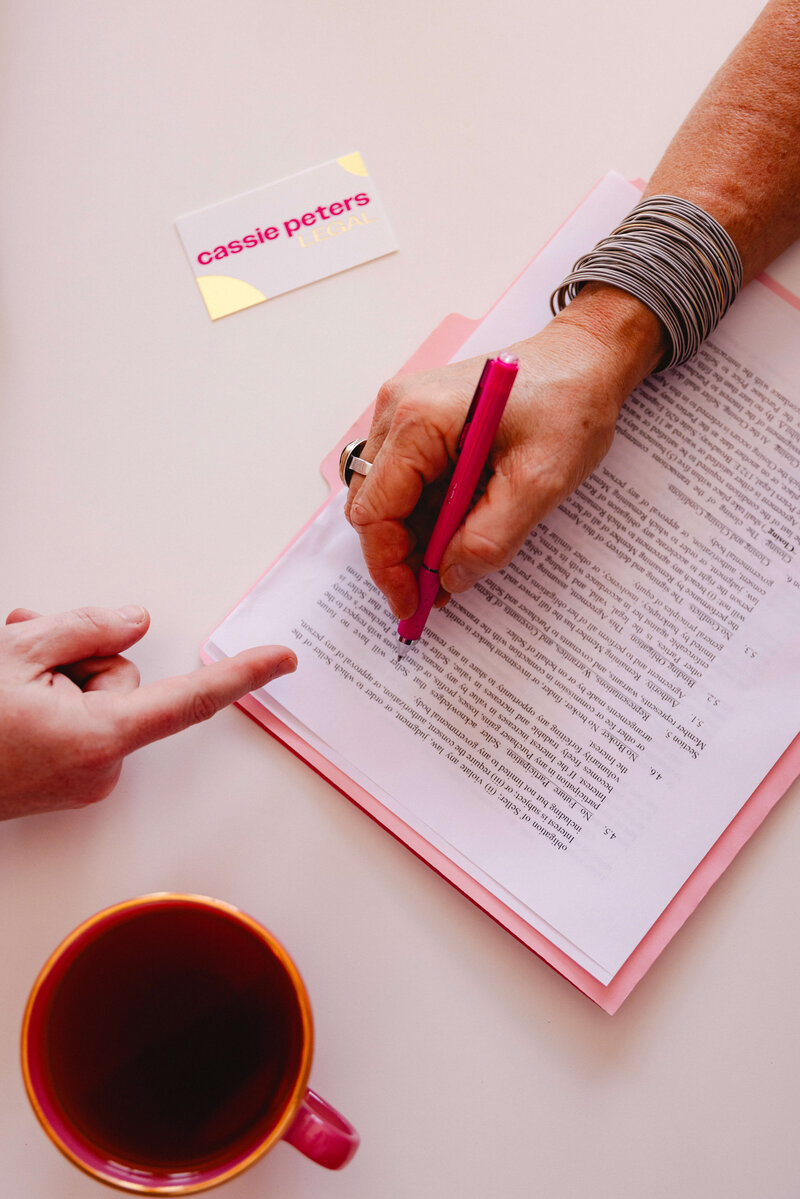 A hand holds a pink pen over a document, representing the legal services Cassie Peters offers to Oregon business owners.