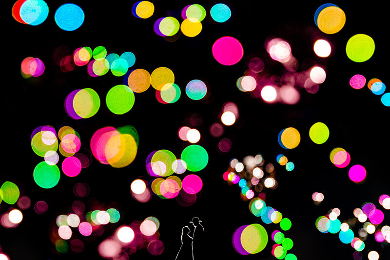 a night time Silhouette of a wedding couple with colorful balls of light in the foreground 