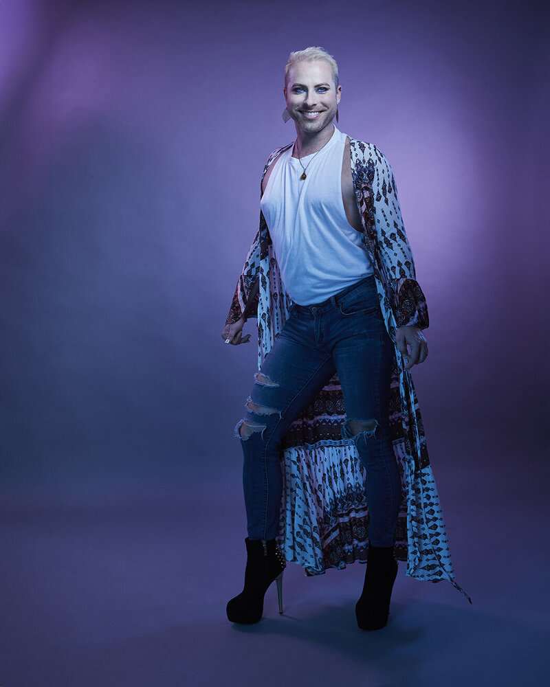Stylized studio portrait of Dain August in a glittering blue outfit, posing confidently with vibrant lighting effects, captured by Ylva Erevall.