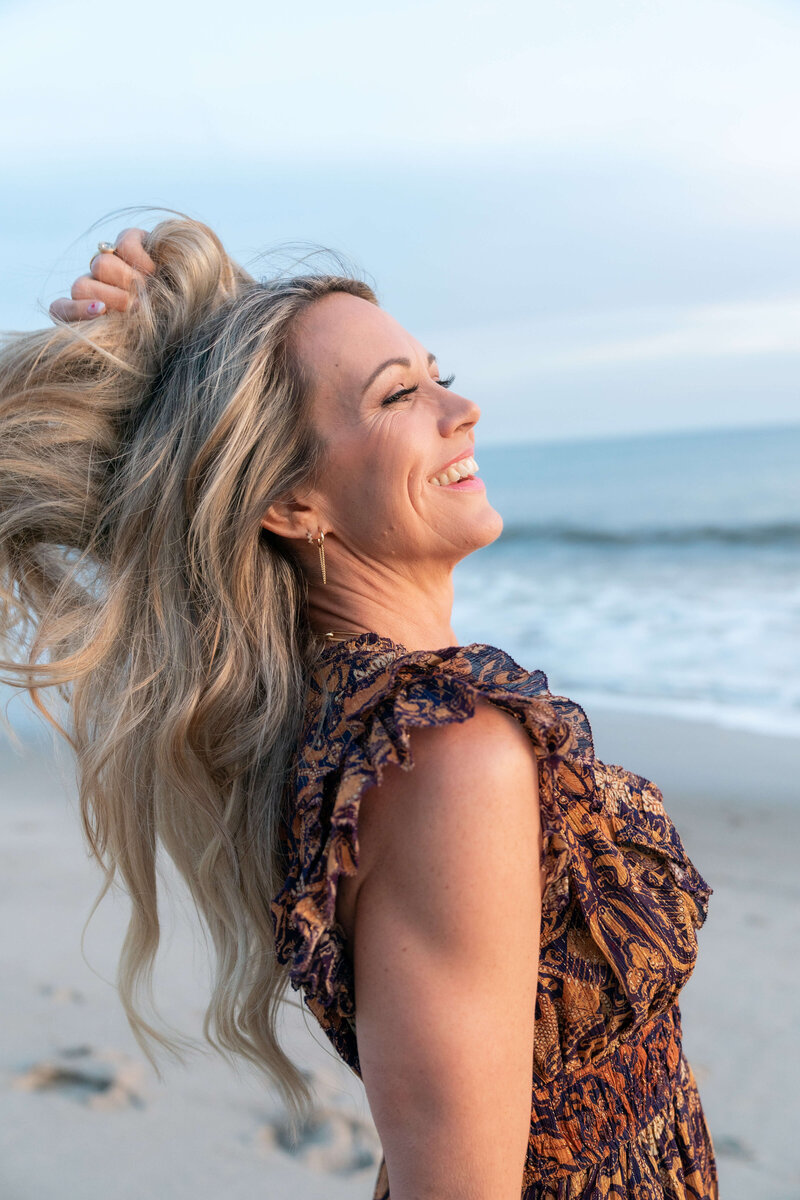 A women life coach on the beach smiling to the sun taking a moment to breath.