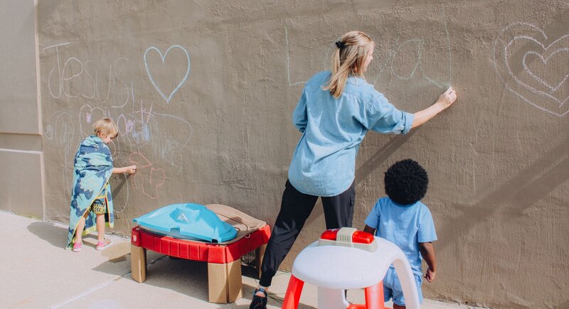 A teacher writing with chalk in front of a daycare child
