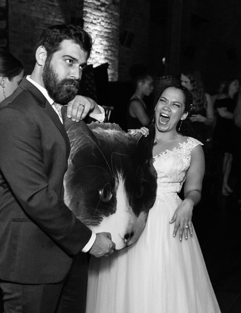 A bride and groom laughing as they hold up a massive printout of a cat's head.