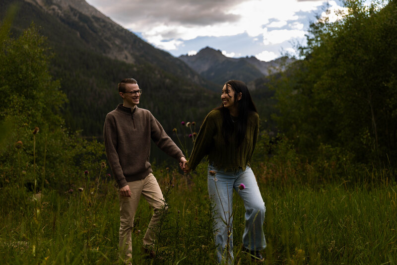 fun couple walking through the tall grass with a mountain view in Colorado
