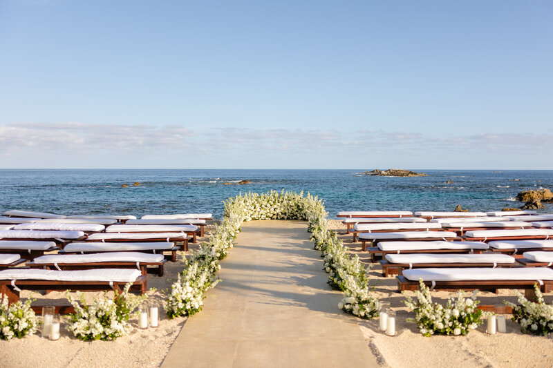A Los Cabos beachfront wedding ceremony space with benches and greenery on either side of a concrete aisle