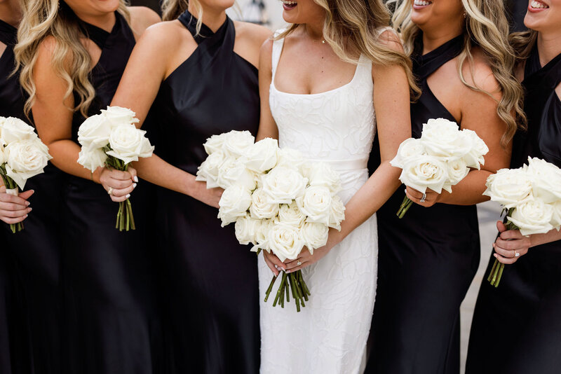 Bride with her bridesmaids in black dresses holding white bouquets