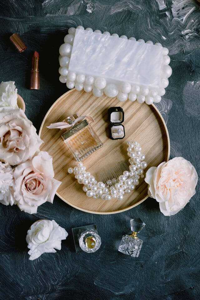 Getting ready photo of Flat lays on a wooden tray, there is a white purse, a necklace, and a pair of earrings arranged elegantly.
