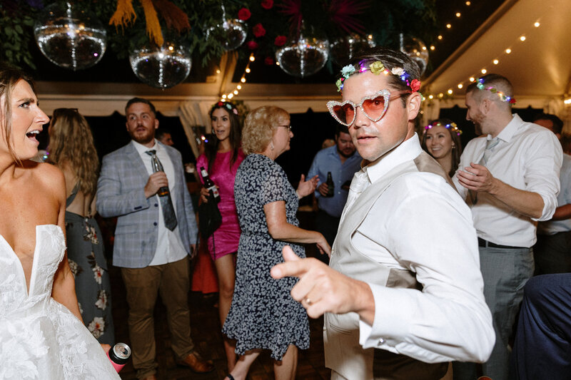 A lively party scene with guests dancing and enjoying drinks, adorned with colorful floral decorations and disco balls overhead.