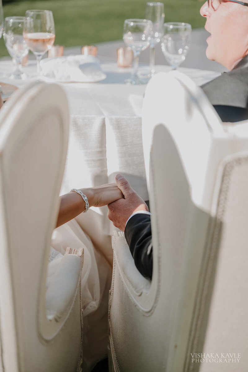 bride and groom holding hands while sitting in large white chairs