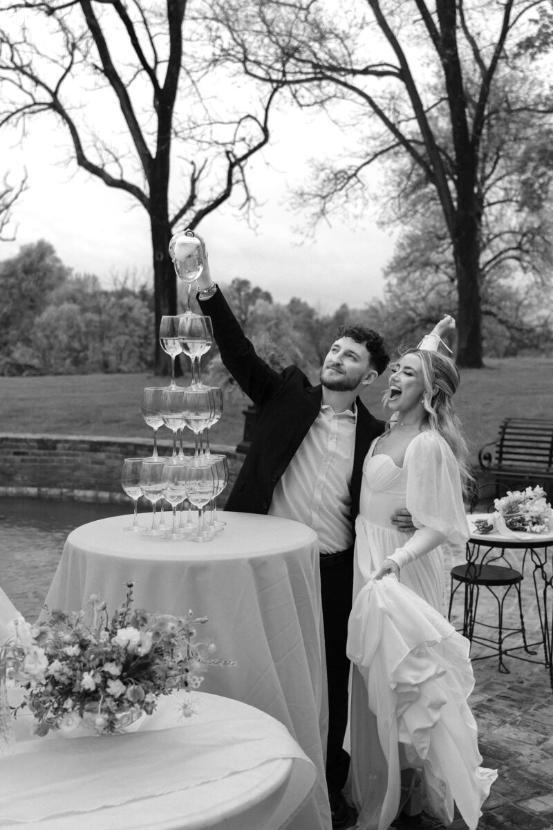 Bride and groom celebrating with a champagne tower at their wedding reception, captured in a joyful moment surrounded by glasses of bubbly.
