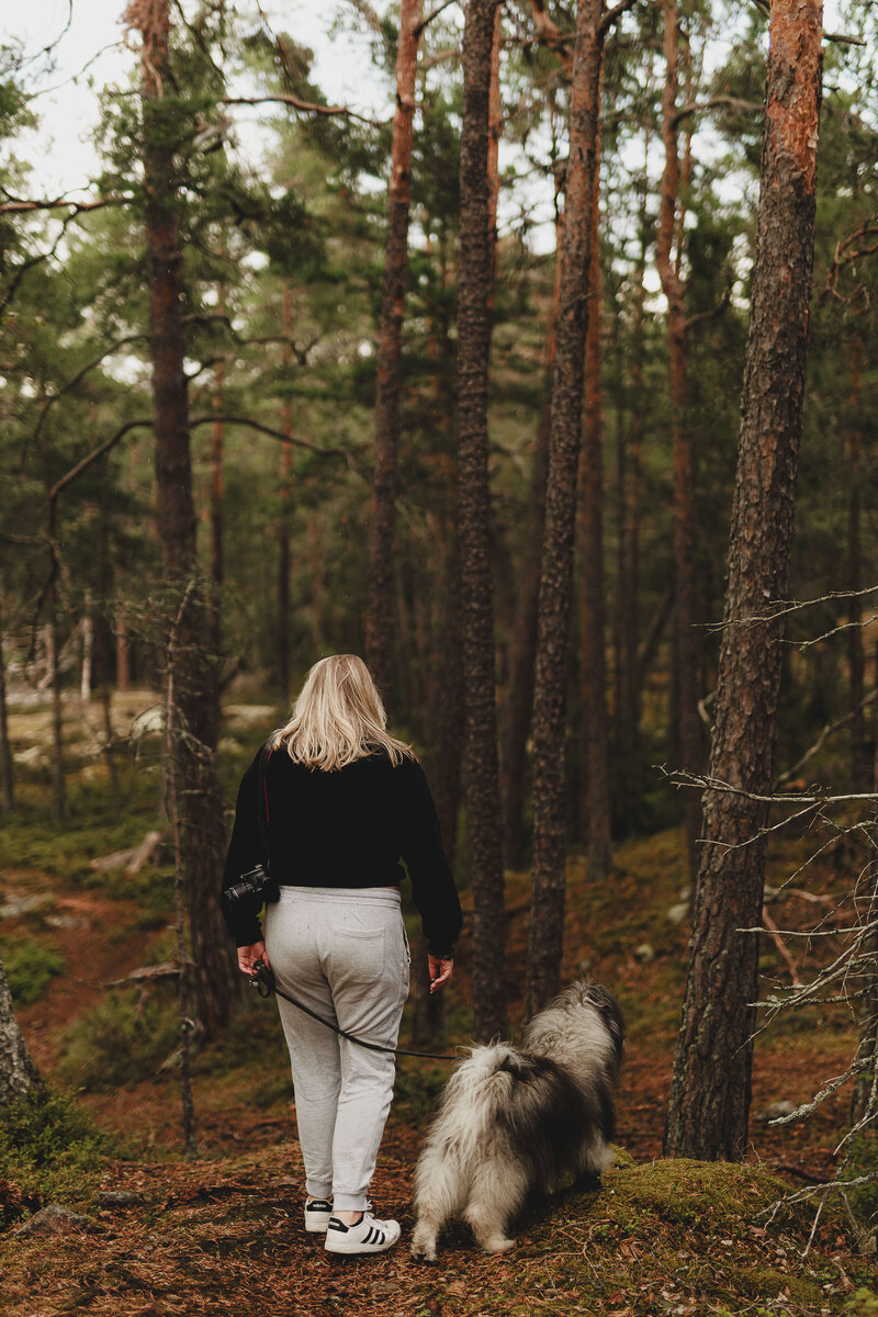 En bild bakifrån på fotografen Fia Wolle och hennes hund Kito gåendes i skogen i Stockholm
