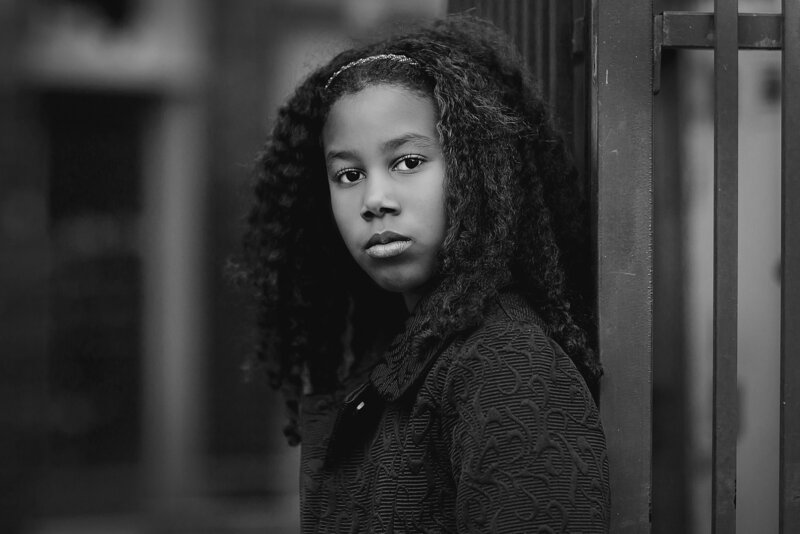 Tween girl in winter coat with a serious look to the camera in black and white.