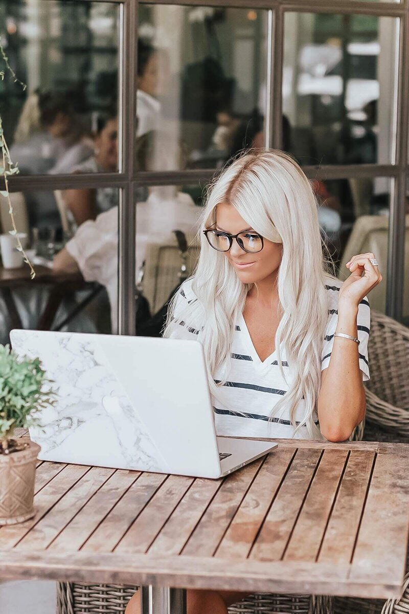 blonde woman sitting outside at a cafe working on her computer and wearing LadyBoss blue light glasses