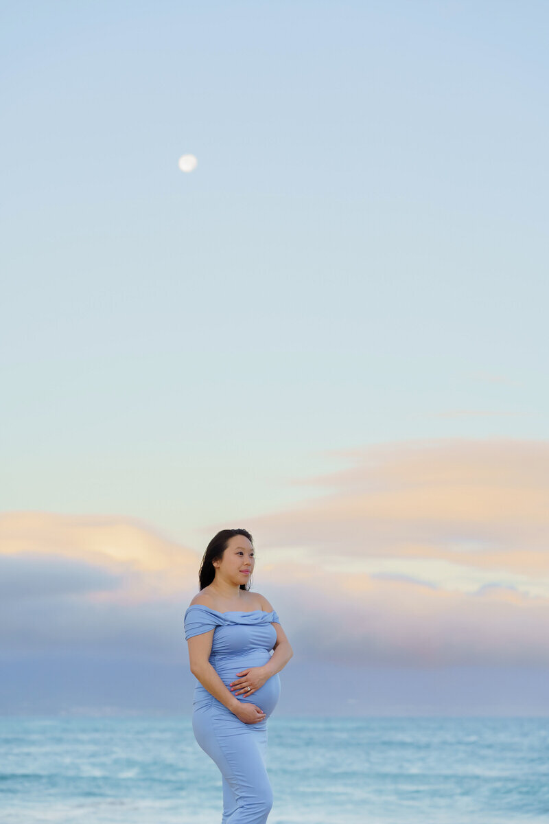 A pregnant woman in a sunrise session with a full moon. Captured by Mariah Milan.