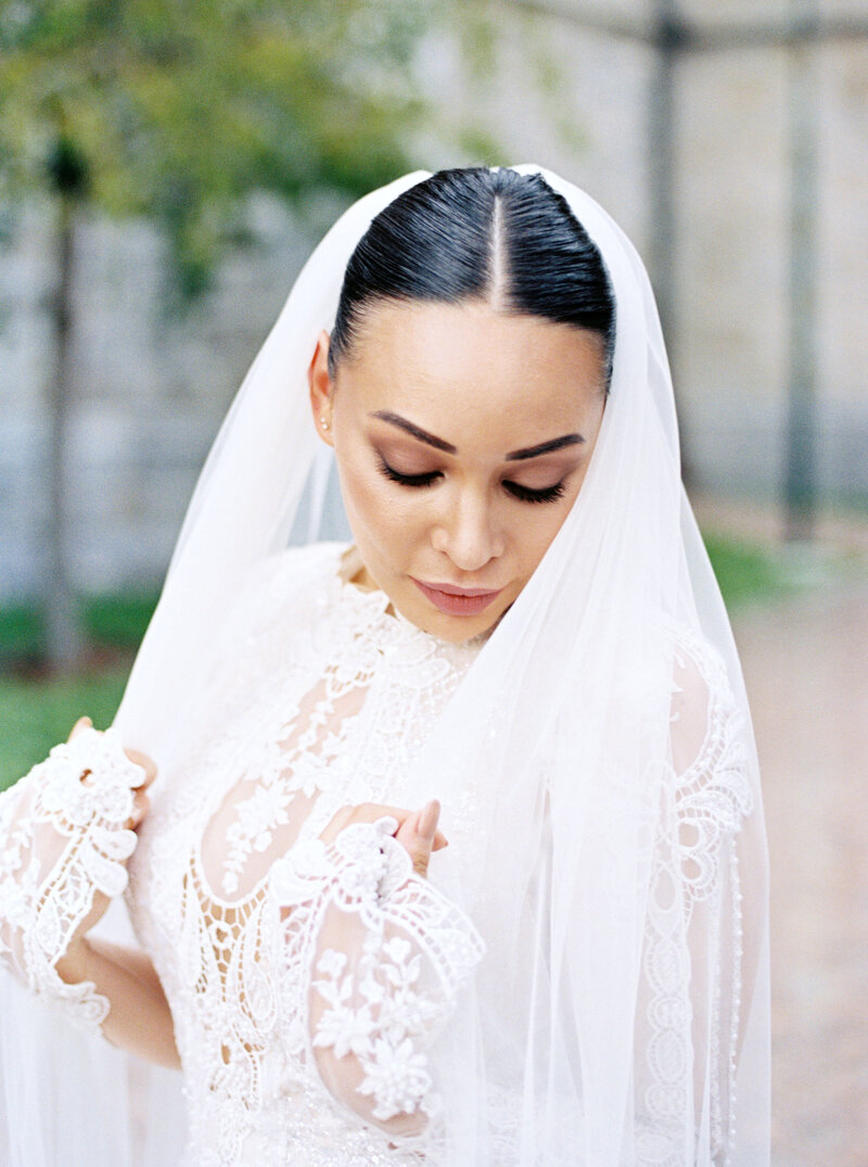 Bride in lace wedding gown and veil looks down over shoulder