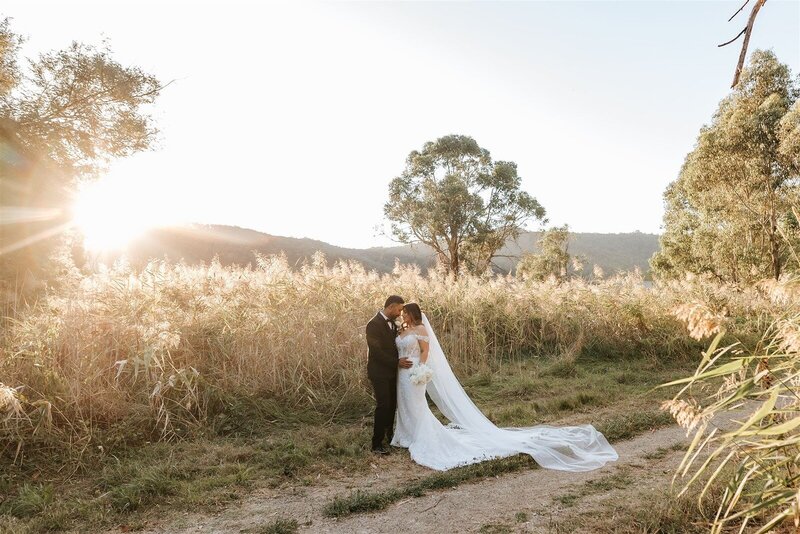 A bride and groom at sunset having wedding photos in a grassy field.