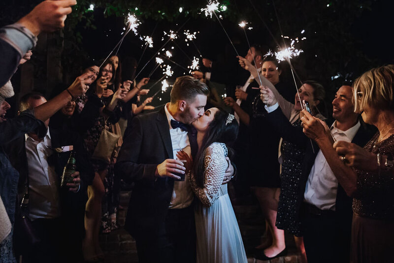 Wedding Photographer, bride and groom kiss underneath sparklers held by friends