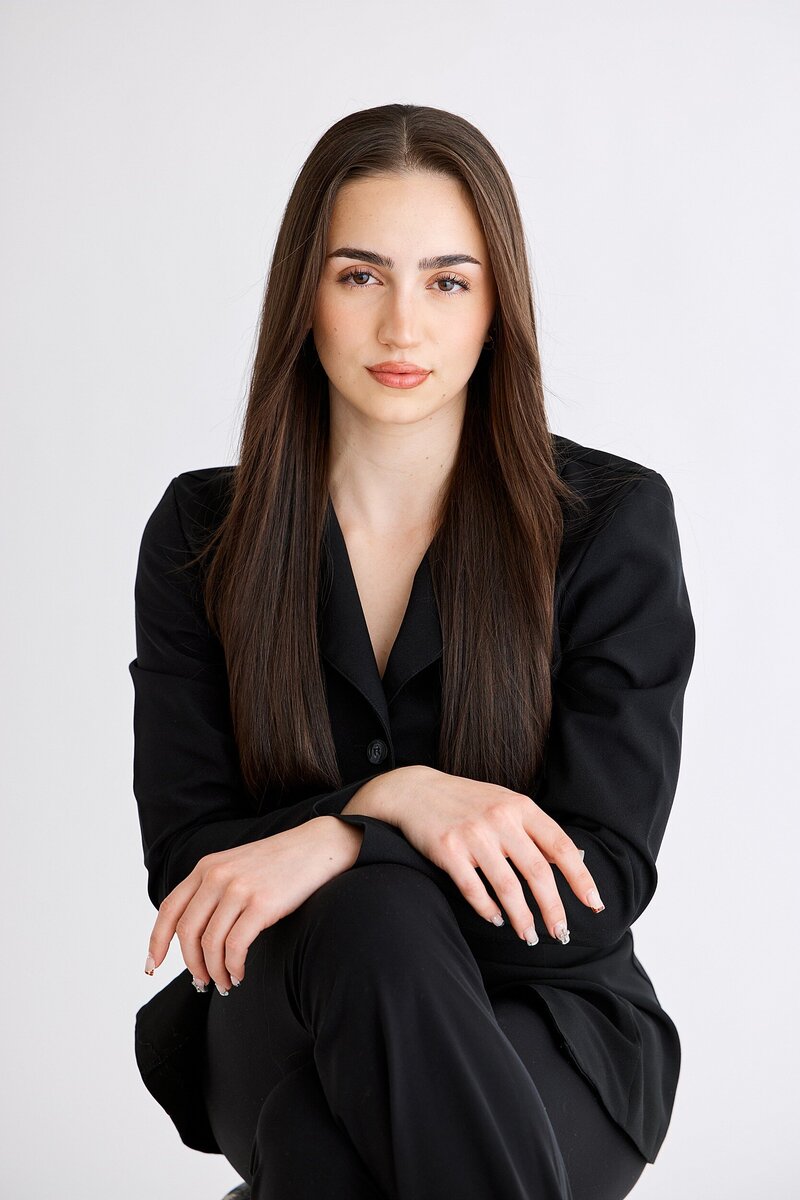Strong and polished headshot of a young woman in an all-black tailored suit sitting confidently, perfect for personal branding or professional use in a modern creative industry.