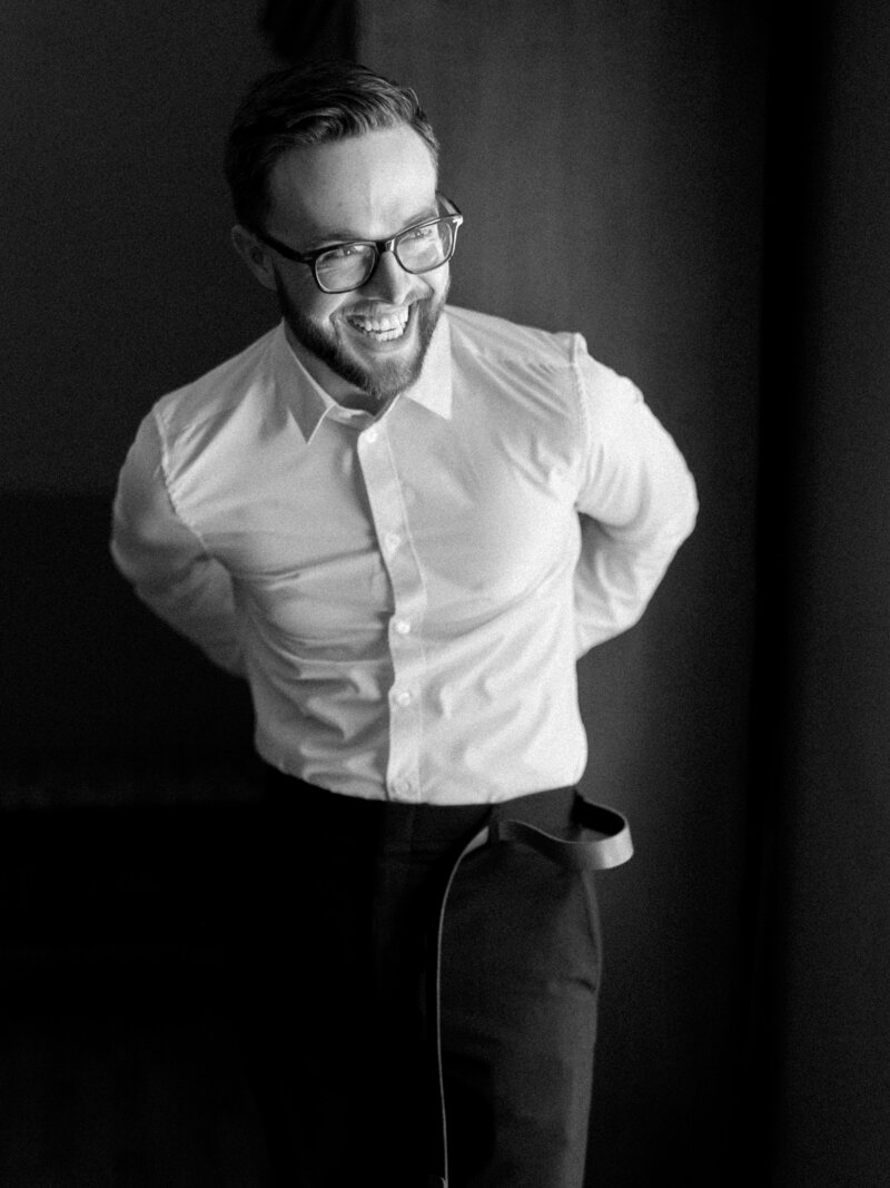 Black and white image of groom putting on his belt