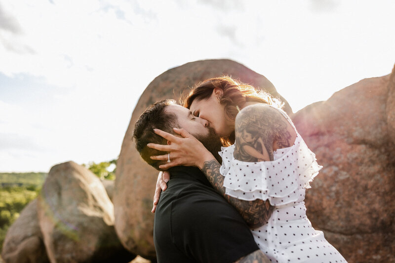 Engagement portrait of a couple at Elephant Rocks in Missouri kissing at sunset. 