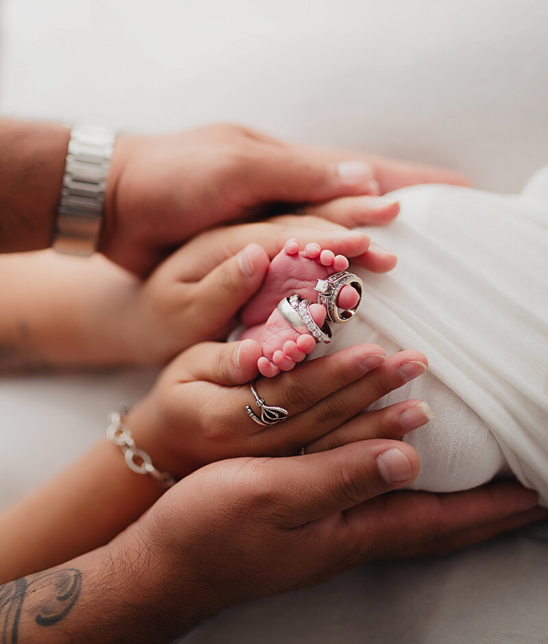 mom and dad hold newborn feet with rings on baby's toes