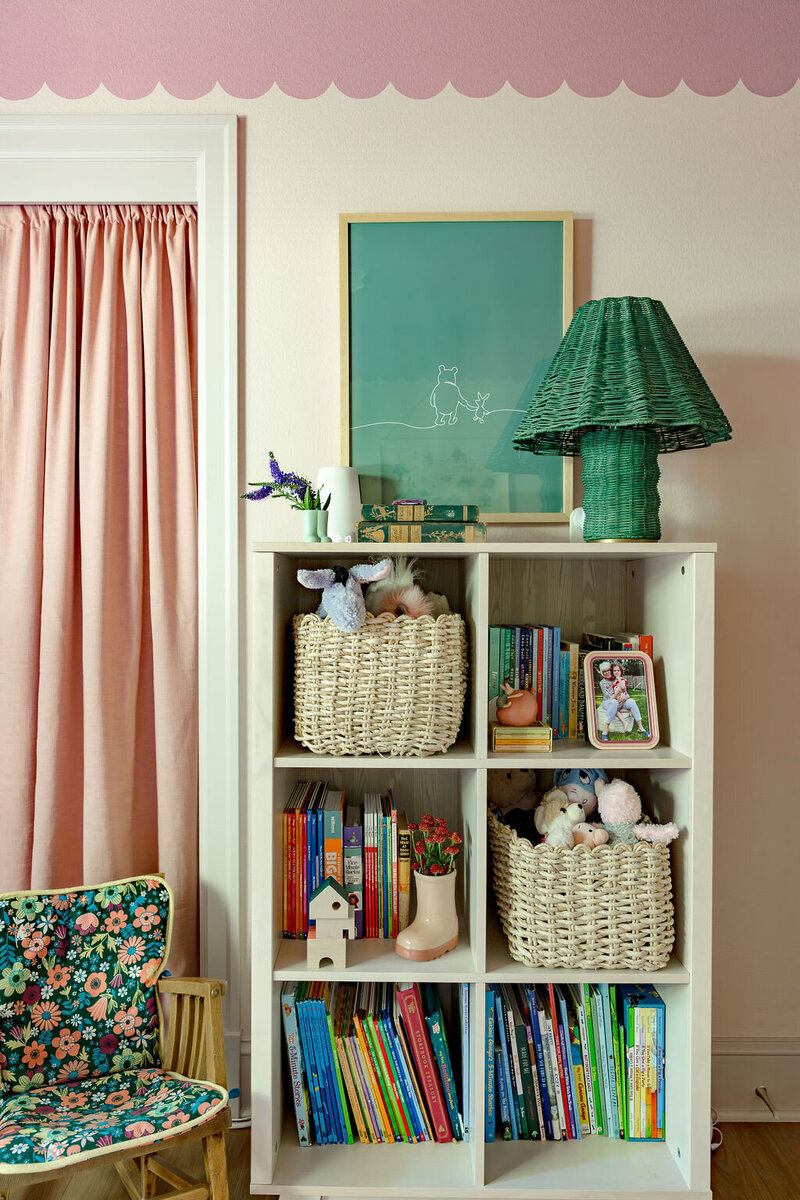 Colorful home decor, knick knacks and books on a shelf, next to a rocking chair with a colorful floral print cushion.
