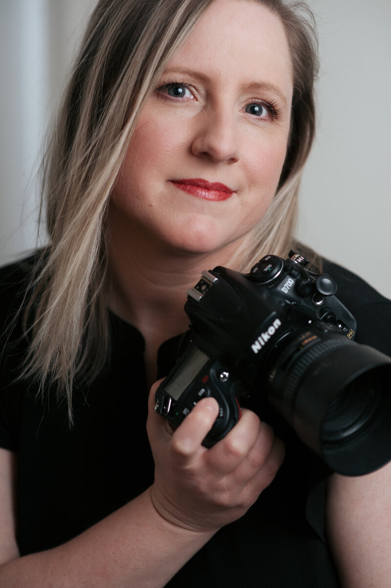 Creative Headshot of Boston personal branding photographer Kristin Palkoner, owner of Lens and Prism Photography, holding her Nikon camera.