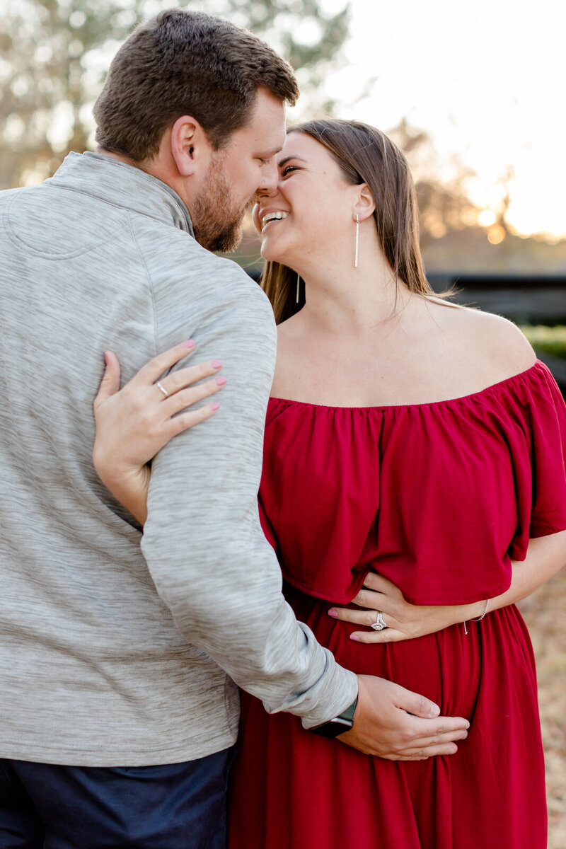 A husband and wife lean in for a kiss as they cradle the new baby bump