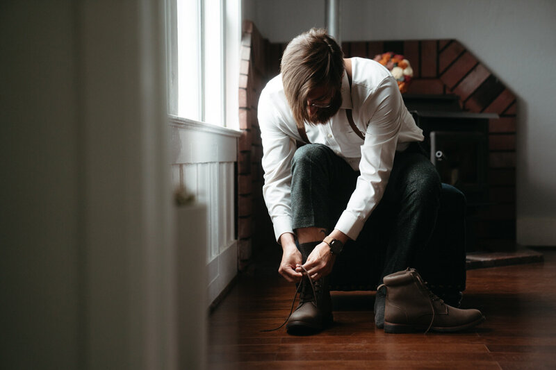 Groom getting ready for his hiking wedding, leaning down to tie his hiking boots 