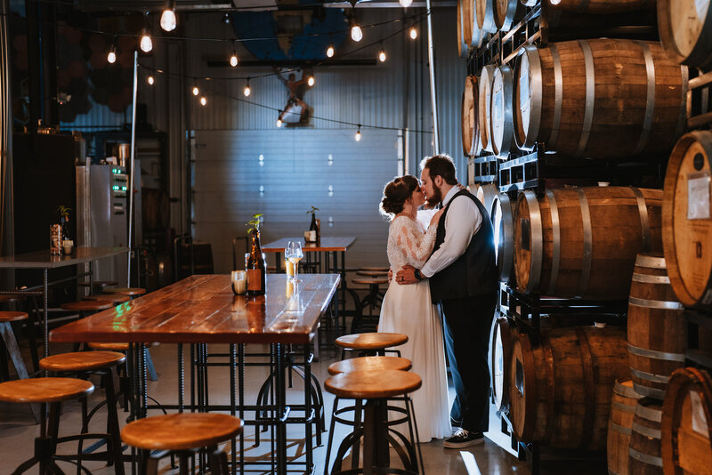 bride and groom kissing while standing in front of oak barrels