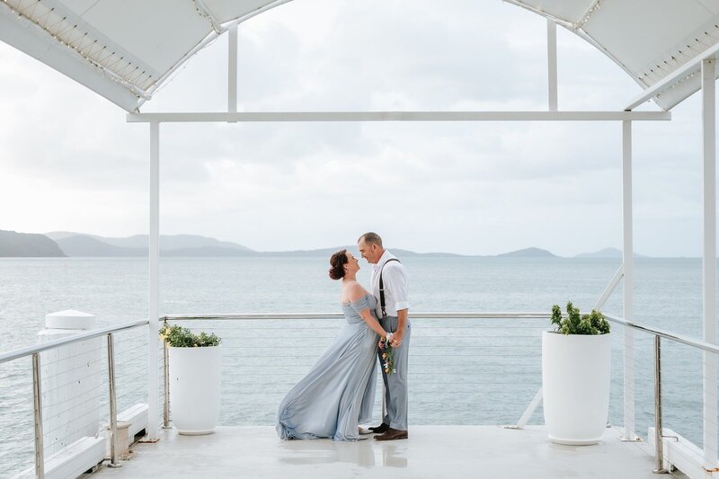A bride in a blue dress and a groom standing on a balcony overlooking the ocean