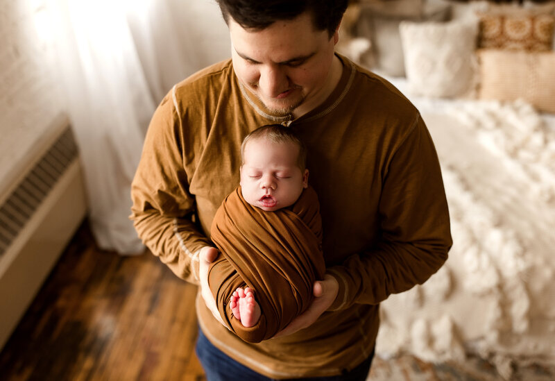 Father holding his baby wrapped in an orange knit swaddle.