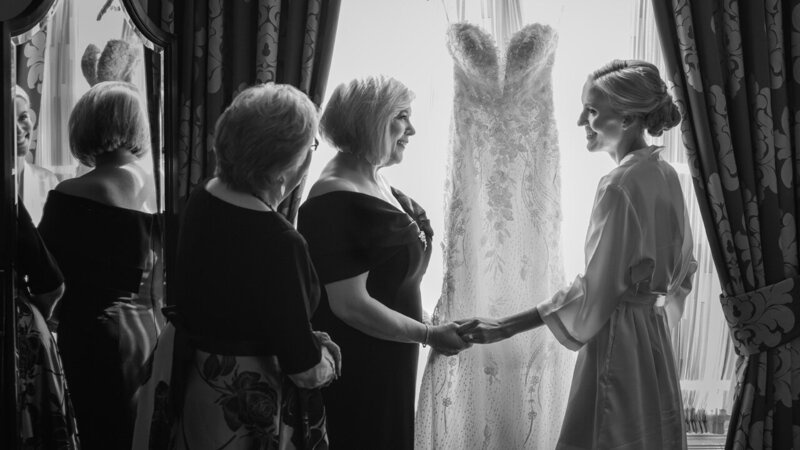 Mother, daughter, and grandmother sharing a heartfelt moment over the wedding gown while getting ready for the big day.