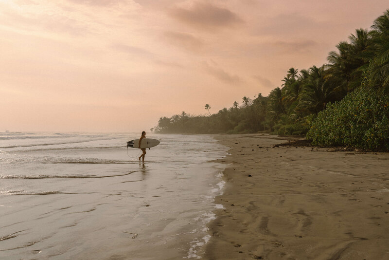 Girl walking down beach with surfboard.