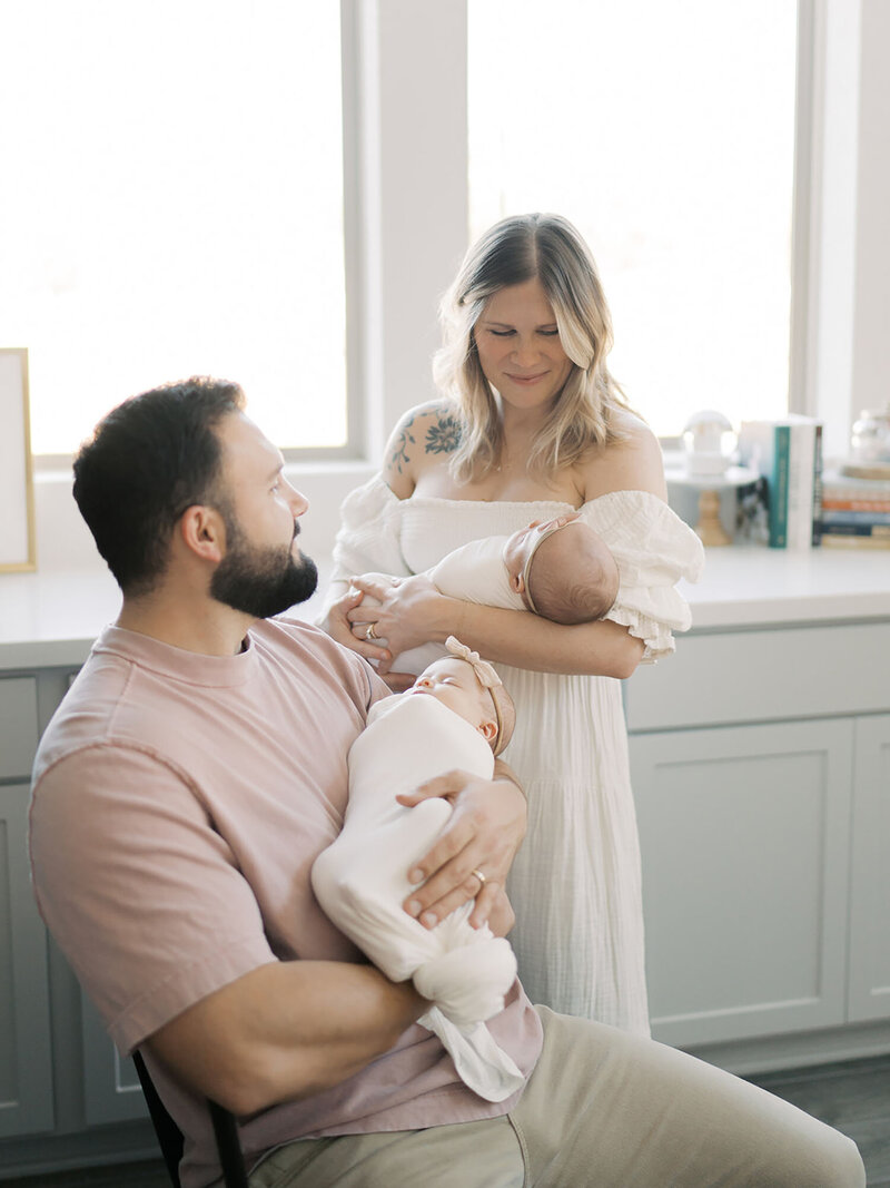 A mother and father are standing together in their kitchen, lovingly holding their newborn twins. The moment, filled with joy and warmth, was captured during a Austin Newborn Portrait Session with Teressa Jane.