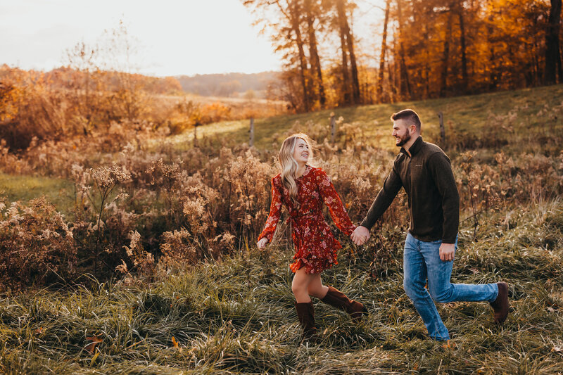 Golden hour wide angle engagement photoshoot with couple holding hands walking through a field of flowers
