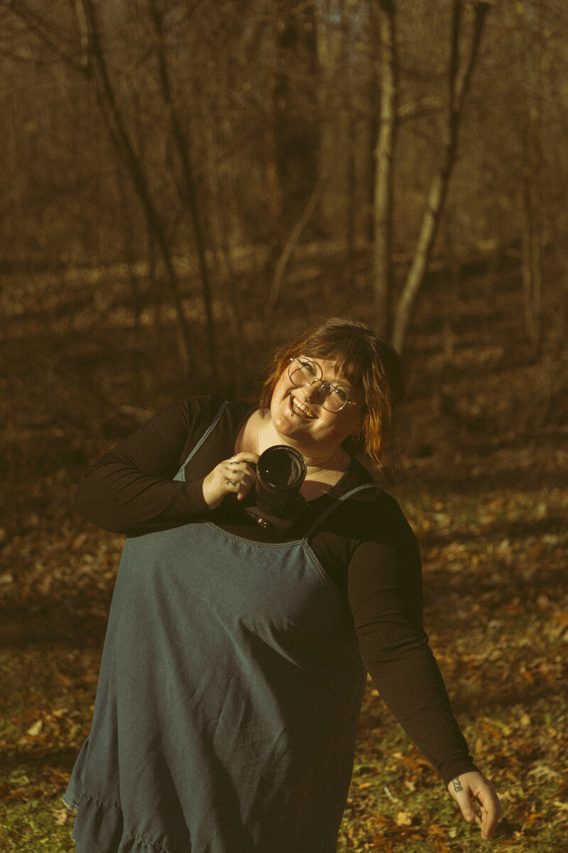 A photographer holds her camera in a snowy forest, smiling at her equipment