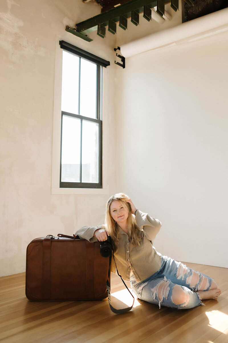 Travel elopement photographer leans on her suitcase, holding her camera and ready for the next adventure. 