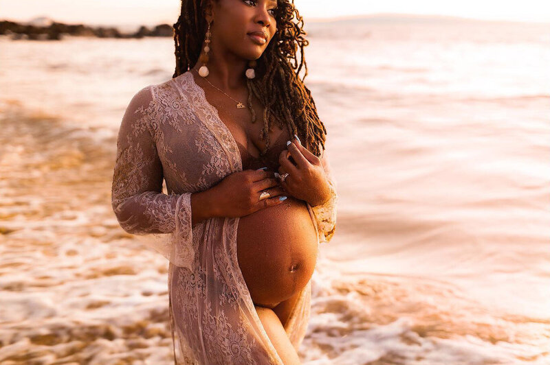 Beautiful pregnant woman photographed by Love + Water on Maui holds her belly and stares out to sea