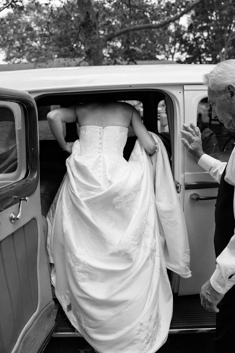 Dramatic gown shot as bride climbs into the back seat of a vintage car on Long Island. 
