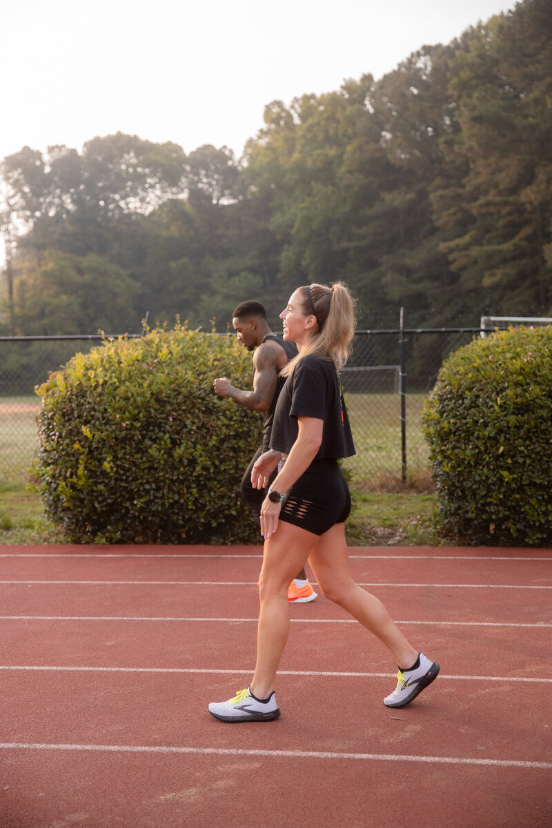 Two athletes walking on a red track surrounded by greenery in Atlanta, GA, during a calm morning workout.