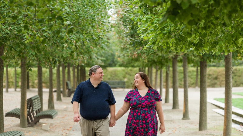 Plus-size couple walking among perfectly manicured trees during their Longwood Gardens engagement photography session, showcasing love and elegance.