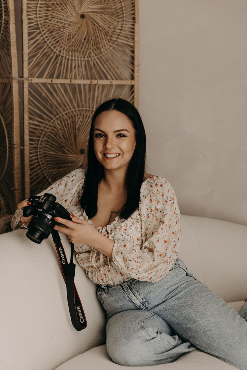 Friendly female photographer in a floral top and jeans holding a camera in her Mullingar studio