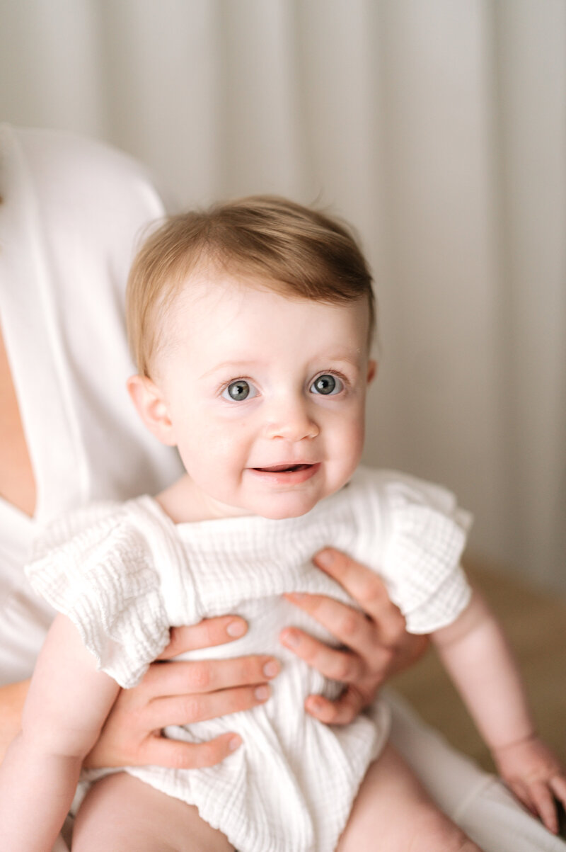 One year old girl sitting on her mums lap smiling at family photoshoot in Horsham
