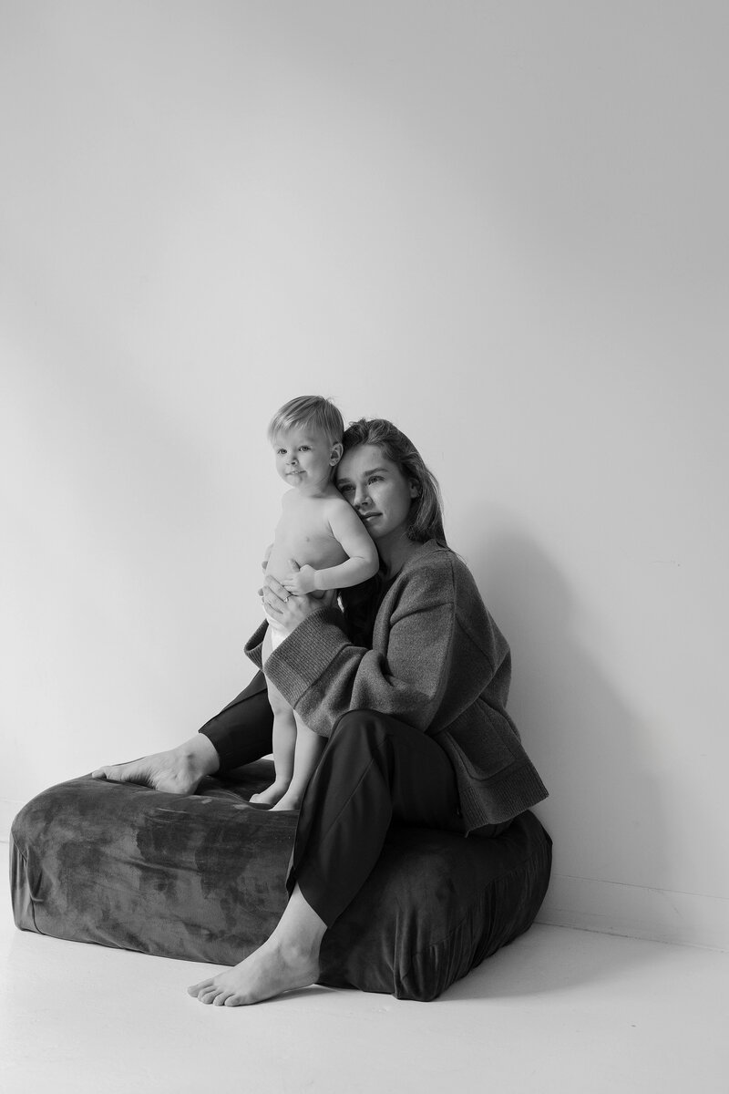 A woman in a tan sweater holds her pregnant belly while posed for an editorial maternity portrait in studio by Boston family portrait photographer, Deborah Zoe.